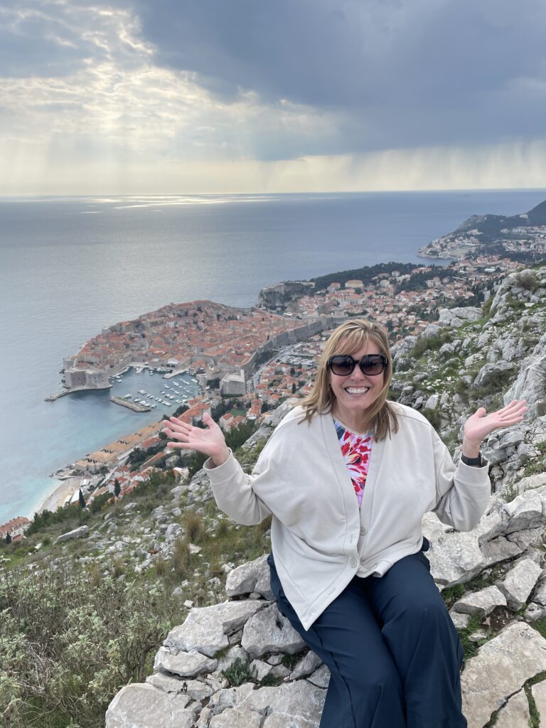 Woman smiling on Mount Srđ overlooking Dubrovnik’s Old Town and the Adriatic Sea.