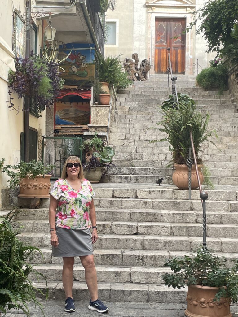 Woman standing on a stone staircase in Taormina near a historic church.