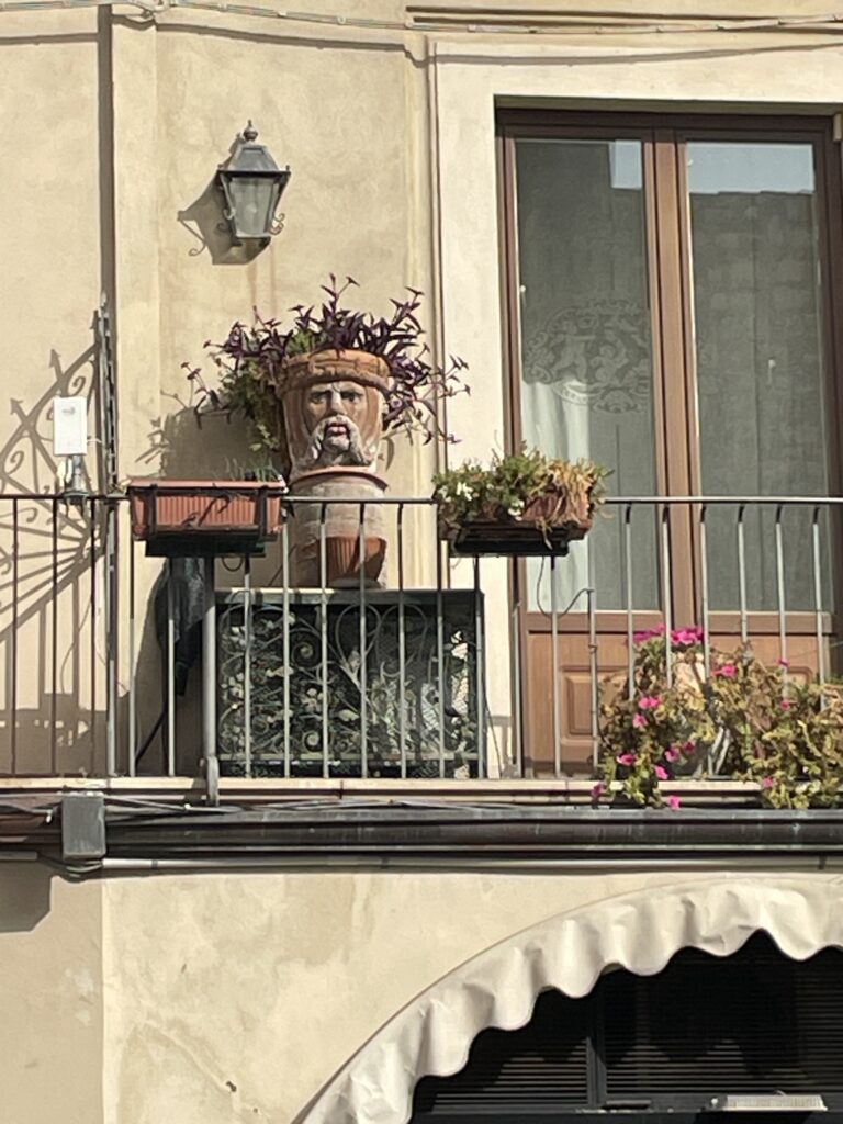 Balcony in Taormina with a Sicilian Testa di Moro head planter and flowers.