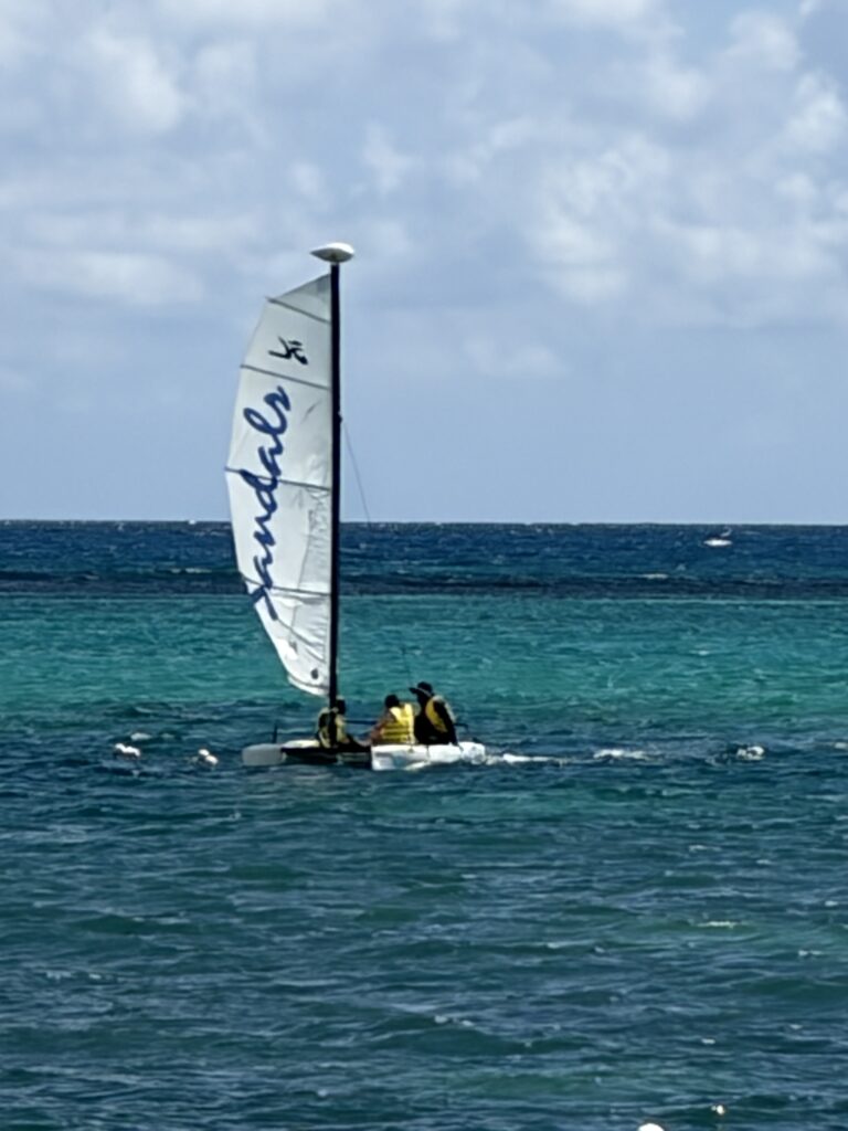 Gallery of water activities at Sandals Dunn’s River in Jamaica, including a Hobie Cat sailboat, a glass-bottom boat excursion, and guests tubing on the Caribbean Sea.